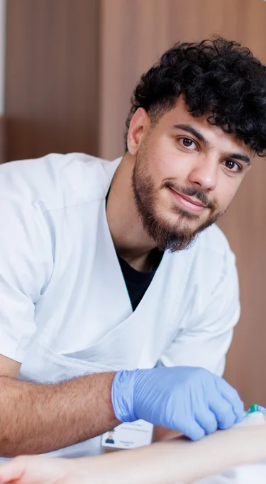 Junger Auszubildender legt Zugang am Arm und lächelt in die Kamera