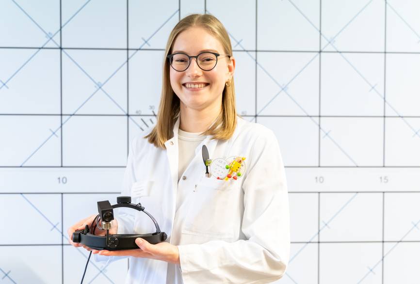 Eine junge Frau, die in der Augenklinik tätig ist, in weißem Kasack hält ein Instrument.