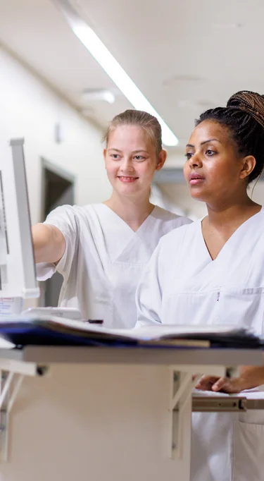 Zwei Auszubildende Bereich Pflege auf einem Flur stehend mit weißen Kasacks.