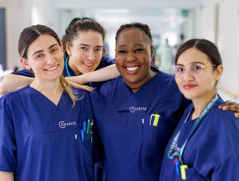 Vier Pflegerinnen, die auf einem Stationsflur stehen und freundlich in die Kamera lächeln