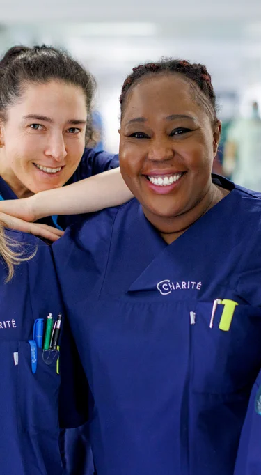 Vier Pflegerinnen, die auf einem Stationsflur stehen und freundlich in die Kamera lächeln