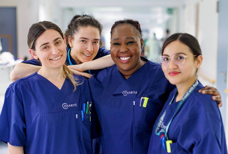 Vier Pflegerinnen, die auf einem Stationsflur stehen und freundlich in die Kamera lächeln