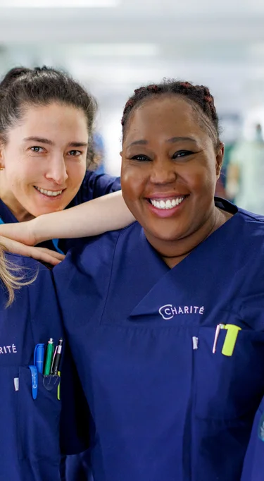 Vier Pflegerinnen, die auf einem Stationsflur stehen und freundlich in die Kamera lächeln