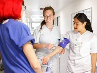 Eine Praxisanleiterin erklärt zwei Pflegeschülerinnen die Messung des Blutdrucks