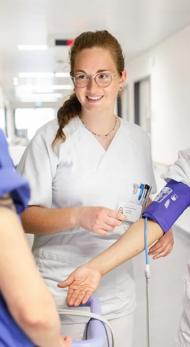 Eine Praxisanleiterin erklärt zwei Pflegeschülerinnen die Messung des Blutdrucks