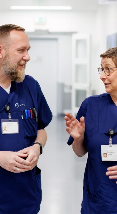 Zwei Personen in Pflege Kasacks laufen den Flur entlang und besprechen sich