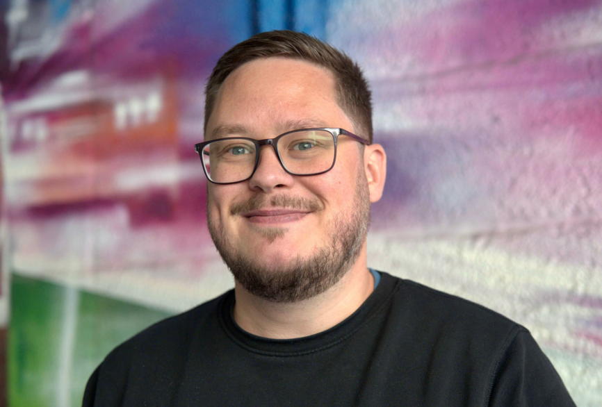 Charité Pflegefachkraft und Zentraler Praxisanleiter Pascal Hunger im Portrait vor einer bunten Grafitti-Wand