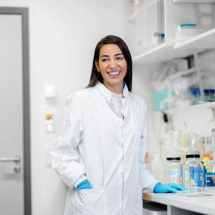 Eine Forscherin steht in einem Labor der Charité und lächelt.