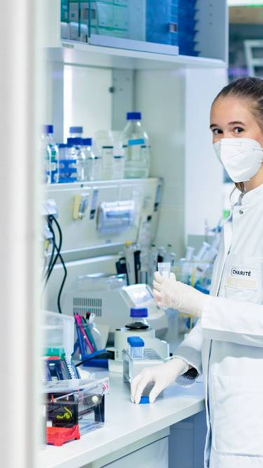 Eine Forscherin steht im Labor und hält ein Zentrifugenröhrchen.