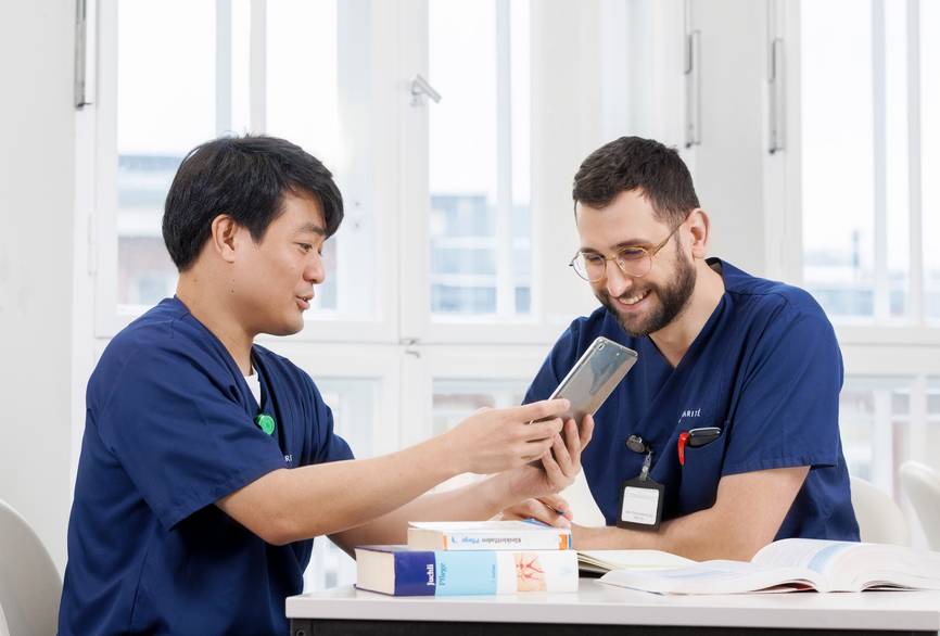 Zwei Pflegende sitzen am Tisch und studieren