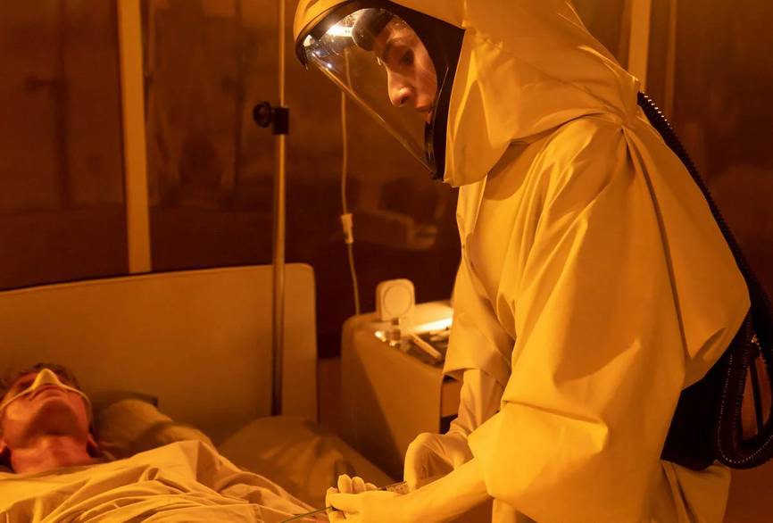 Person mit Schutzkleidung steht an einem Patientenbett