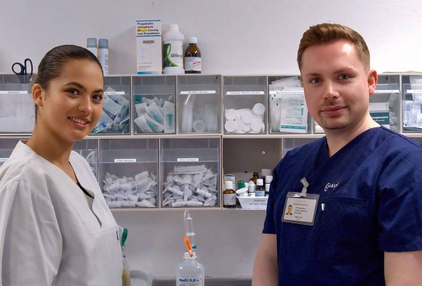 Charité Pflegefachkraft Peter Pflegepool und Auszubildende Arbeitsfläche Charité Pflegefachkraft Peter aus dem Pflegepool mit Auszubildender vor der Arbeitsfläche im reinen Arbeitsraum