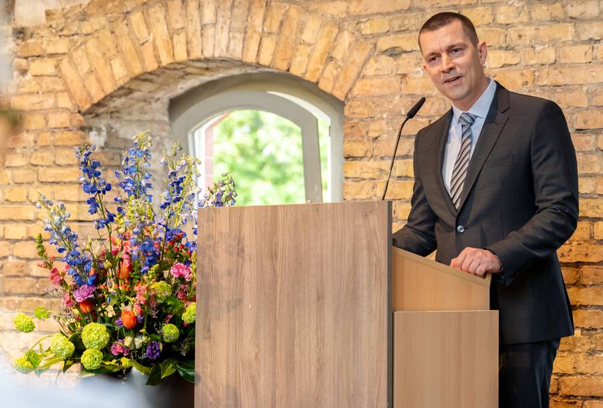 Bei der Abschlussfeier des Pflegebachelors hält ein Mann im Anzug eine Rede an einem Pult.