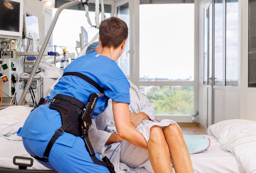 Eine Pflegerin trägt ein Exoskelett und hebt eine Patientin im Bett