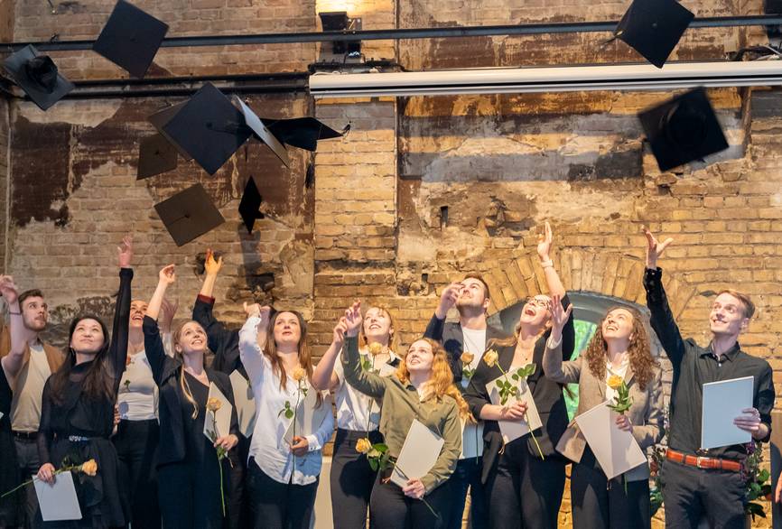 Viele junge Menschen feiern ihren Abschluss und werfen Hüte in die Luft.
