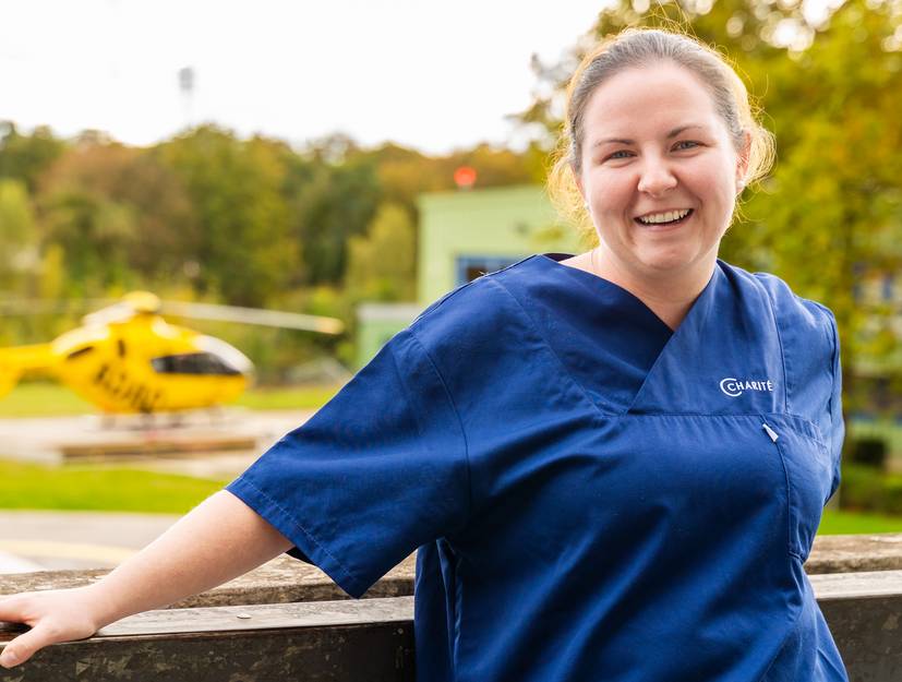 Foto einer jungen Pflegerin des Charité Pflegepools, im Hintergrund ein Rettungshubschrauber