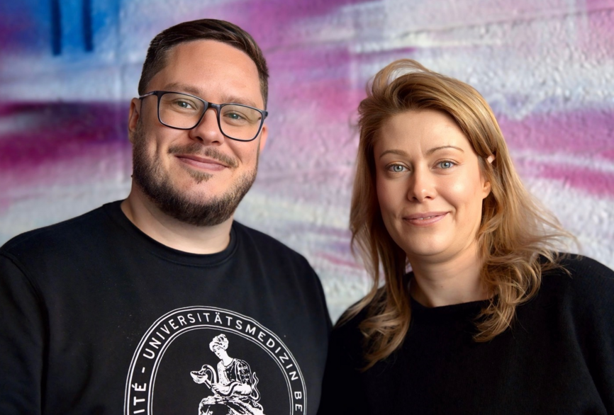 Charité Pflegefachkraft und Zentraler Praxisanleiter Pascal Hunger mit einer Master-Studentin vor einer bunten Graffiti-Wand im Portrait