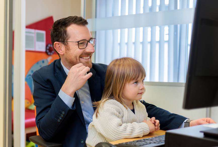 Ein Vater und seine Tochter sitzen an einem Schreibtisch im Eltern-Kind-Zimmer der Charité.