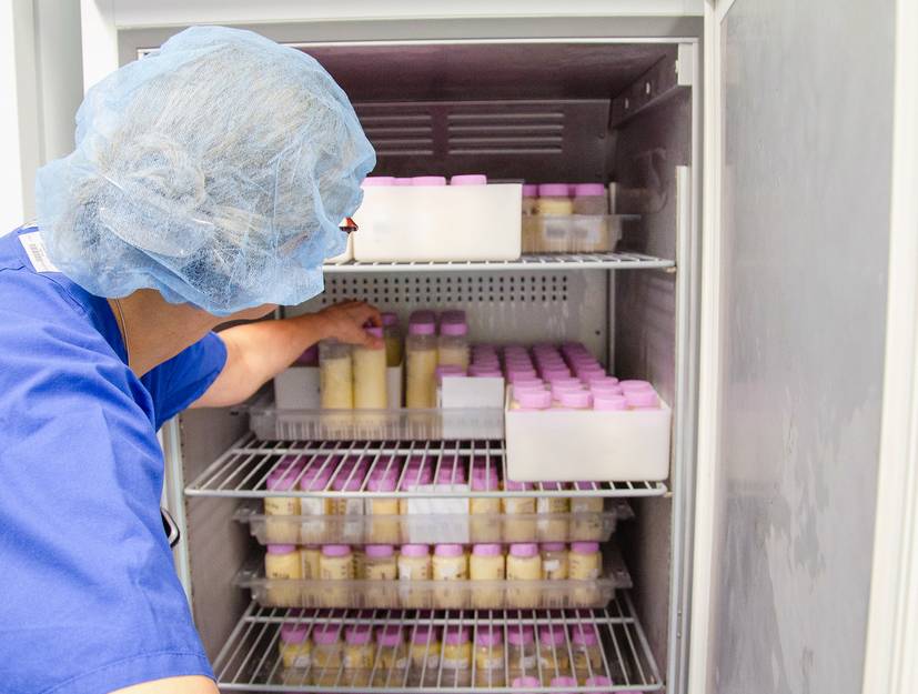 Ein Mitarbeiter steht vor einem Kühlschrank mit Milch gefüllten Gefäßen. 