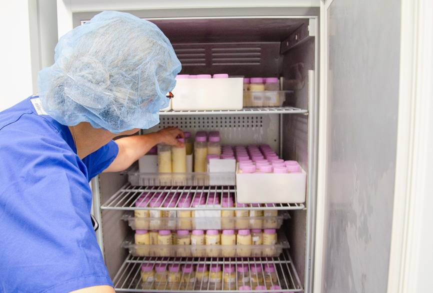 Ein Mitarbeiter steht vor einem Kühlschrank mit Milch gefüllten Gefäßen. 