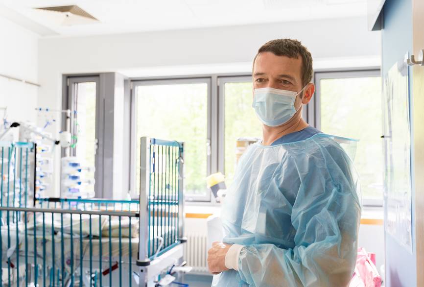 Ein Pfleger mit Mundschutz und Schutzkittel auf der Kinderintensivstation.