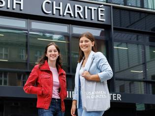 Zwei junge Auszubildende stehen vor dem Charité-Gebäude und lächeln  