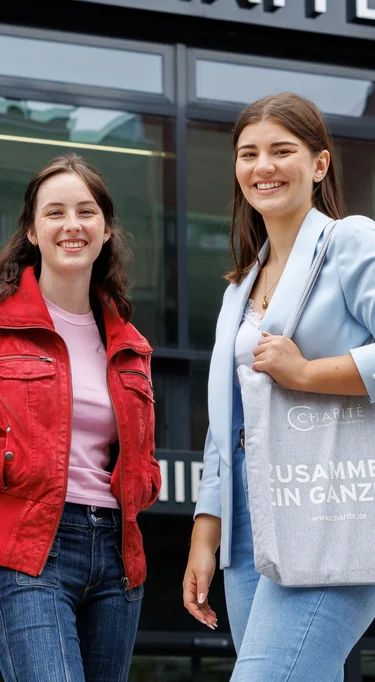 Zwei junge Auszubildende stehen vor dem Charité-Gebäude und lächeln  