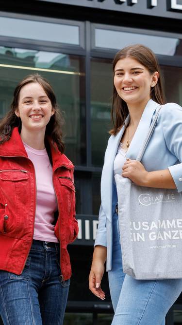 Zwei junge Auszubildende stehen vor dem Charité-Gebäude und lächeln  