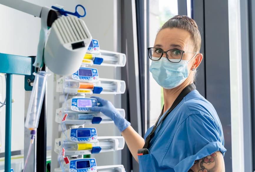 Eine Pflegerin steht im Zimmer mit Mundschutz und schaut in die Kamera.