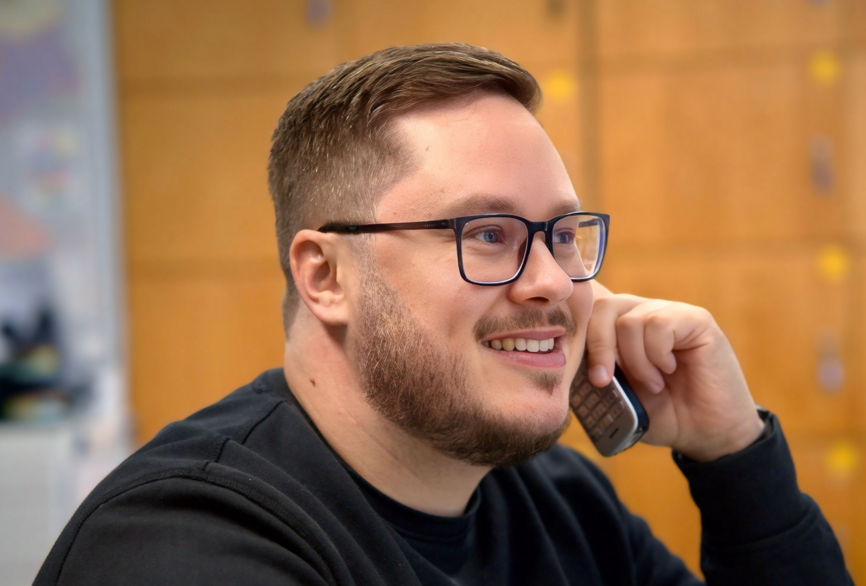 Charité Pflegefachkraft und Zentraler Praxisanleiter Pascal Hunger lächelnd am Telefon im Gespräch