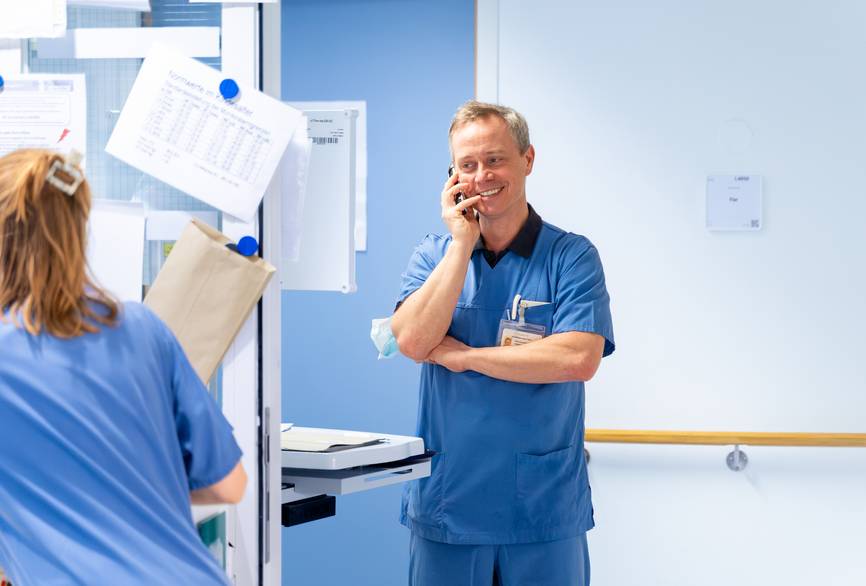 Zwei Pflegekräfte in blauen Kasacks unterhalten sich.